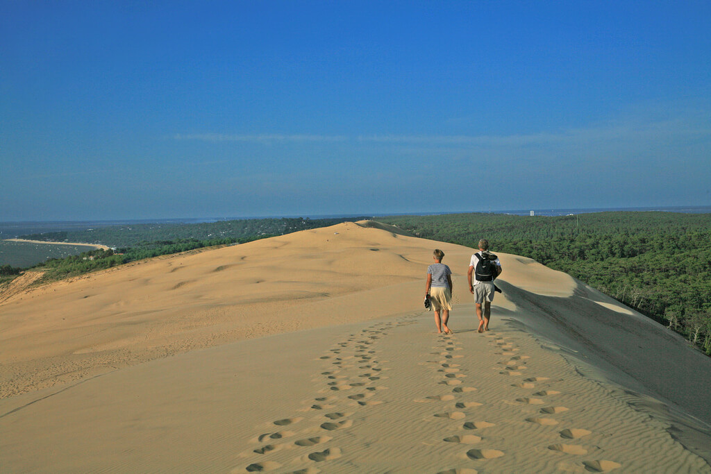 Мужчина и женщина идут по большой песчаной дюне.