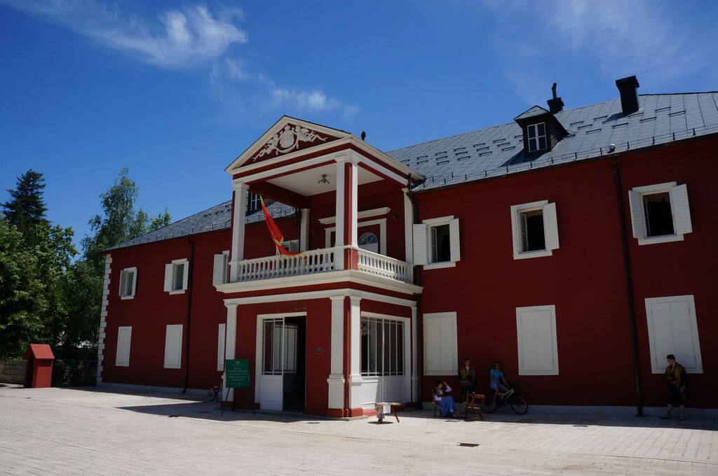 Фасад красного двухэтажного здания с крыльцом и балконом в центре.