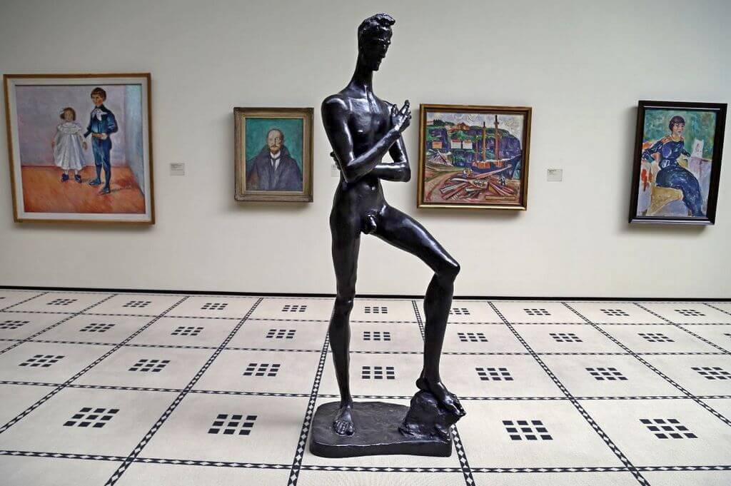 Статуя худого мужчины на фоне четырех картин в музее.