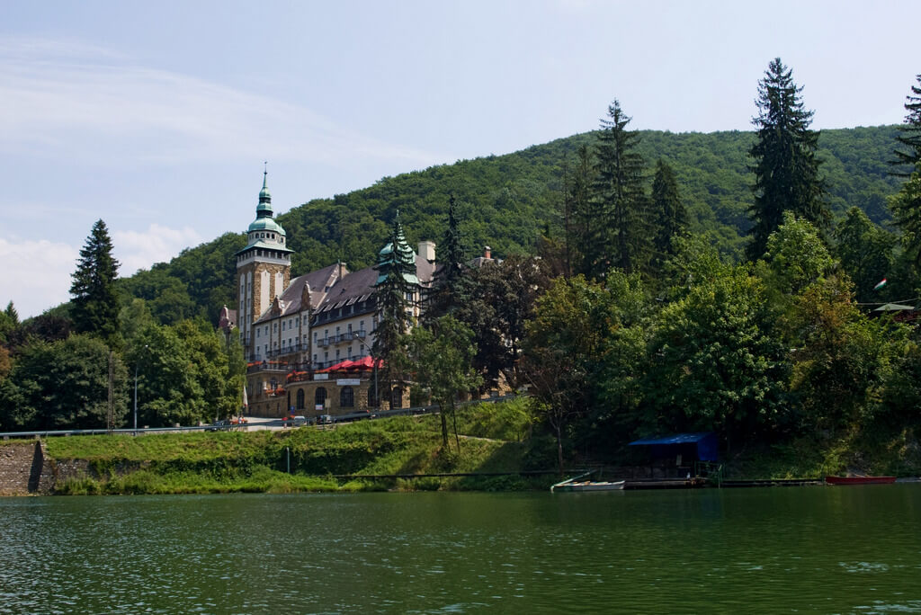Замок у озера на фоне большого заросшего деревьями холма.