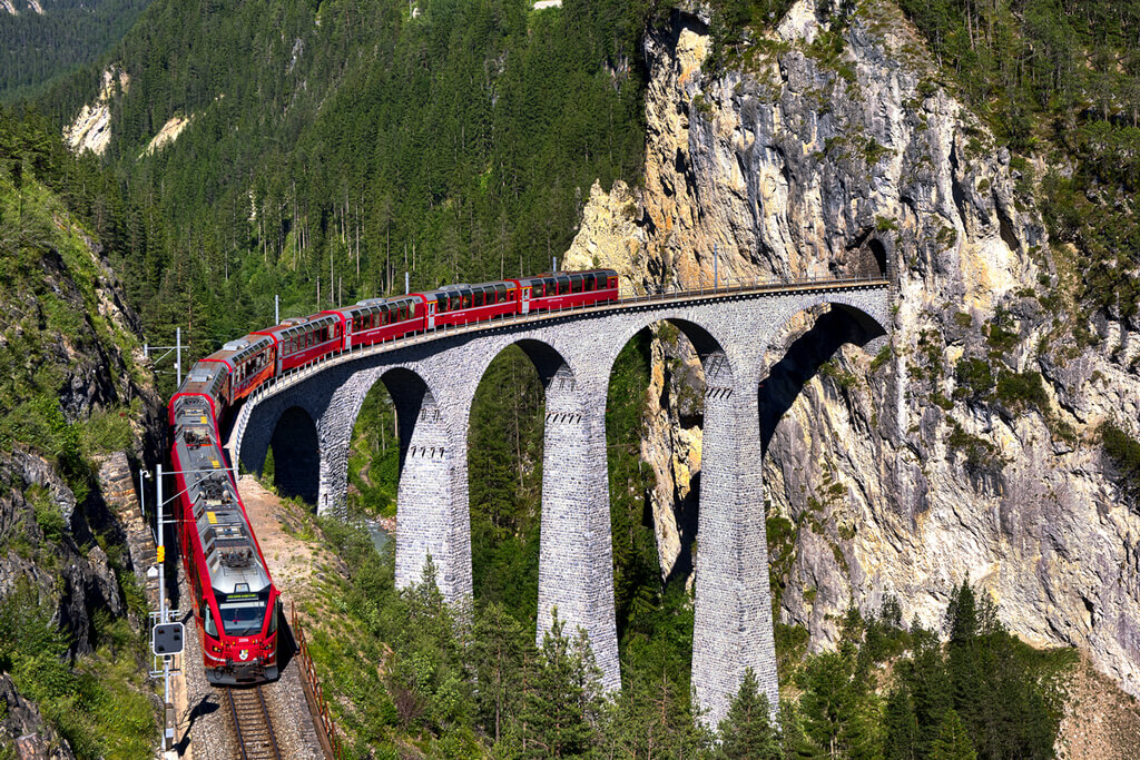 Железнодорожный мост в горах и поезд выезжающий из тоннеля.