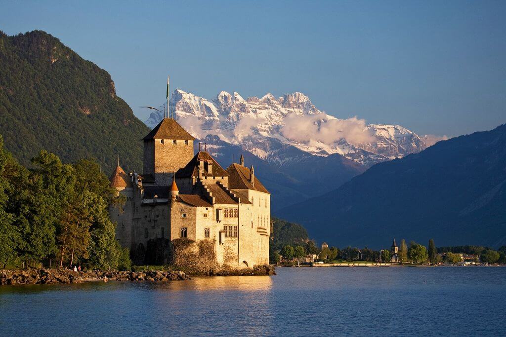 Средневековый замок на берегу озера, на фоне заснеженных гор.