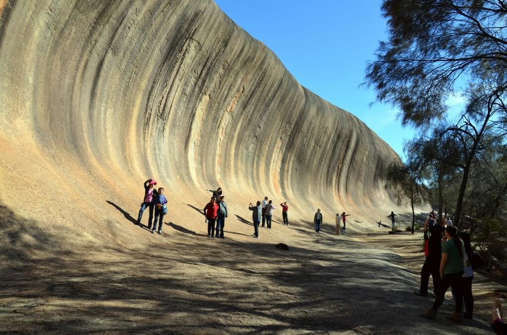 Туристы фотографируются у небольшой изогнутой скалы.