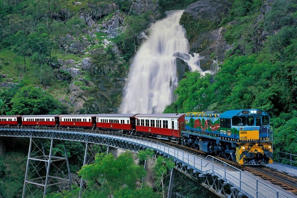Поезд едет по мосту на фоне водопада.